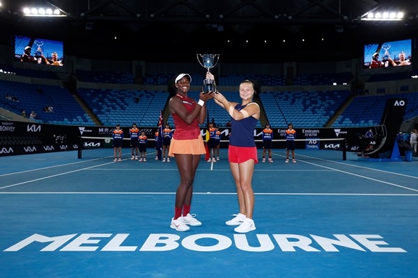 Clervie Ngounoue and Diana Shnaider with the Australian Open girls' doubles trophy in an empty stadium.