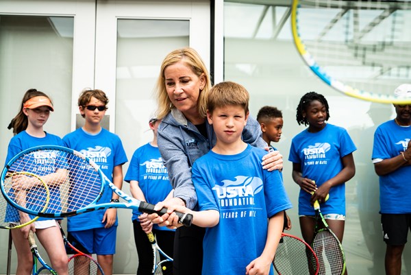 Chris Evert, USTA Foundation chairperson, teaching a child how to hold a tennis racquet and a Rally to Rebuild event in Philadelphia, PA.