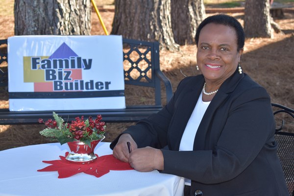 Peggie Henderson, executive director of Family Biz Builder, sitting at a table with a sign that says "Family Biz Builder"