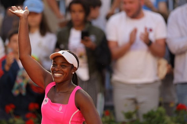 Sloane Stephens waving in a pink top at Roland Garros with a crowd behind her.